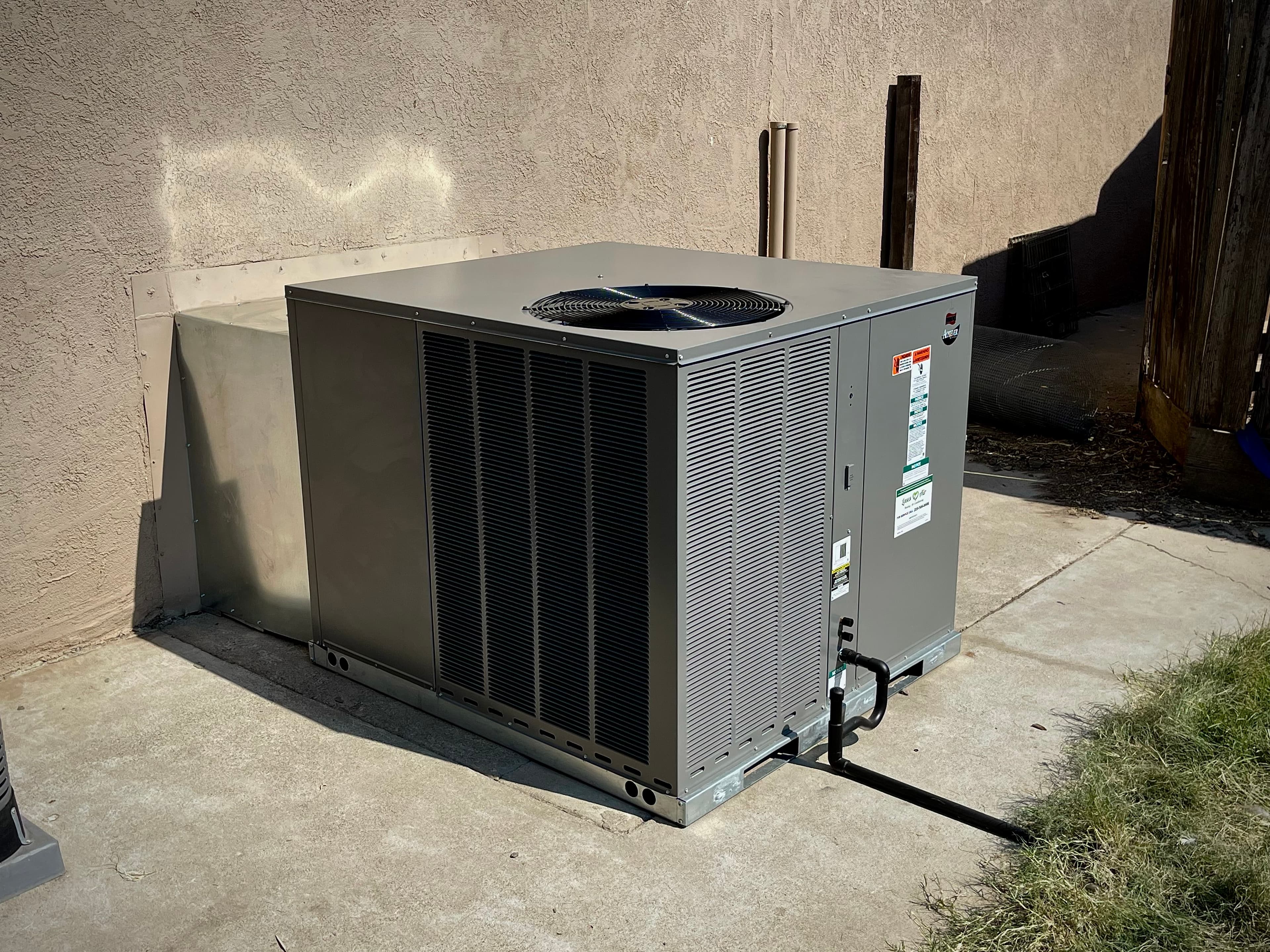 Large grey outdoor HVAC unit installed on a concrete pad against a tan stucco wall.