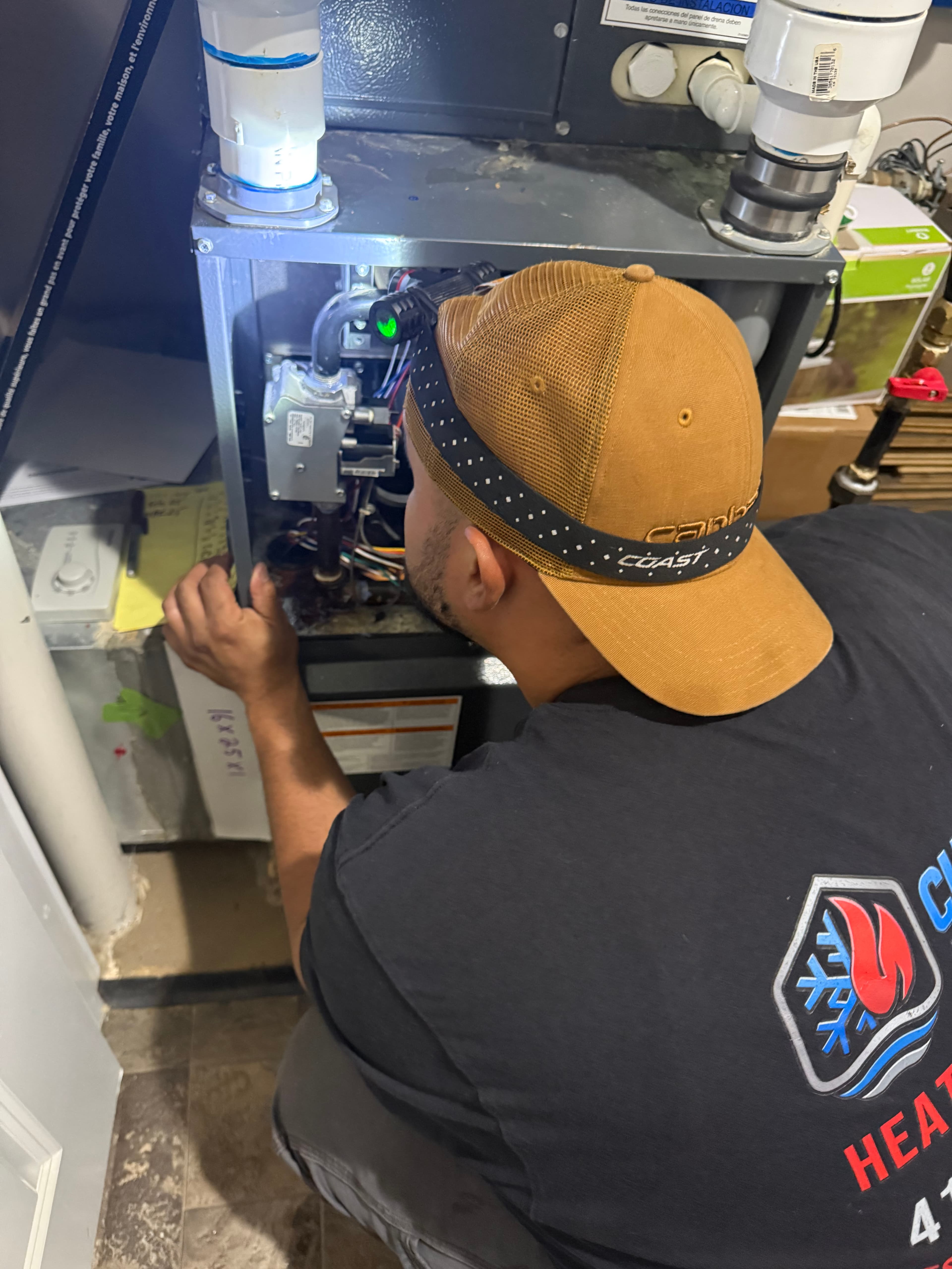 HVAC technician wearing a headlamp inspects the internal components of a residential furnace unit.