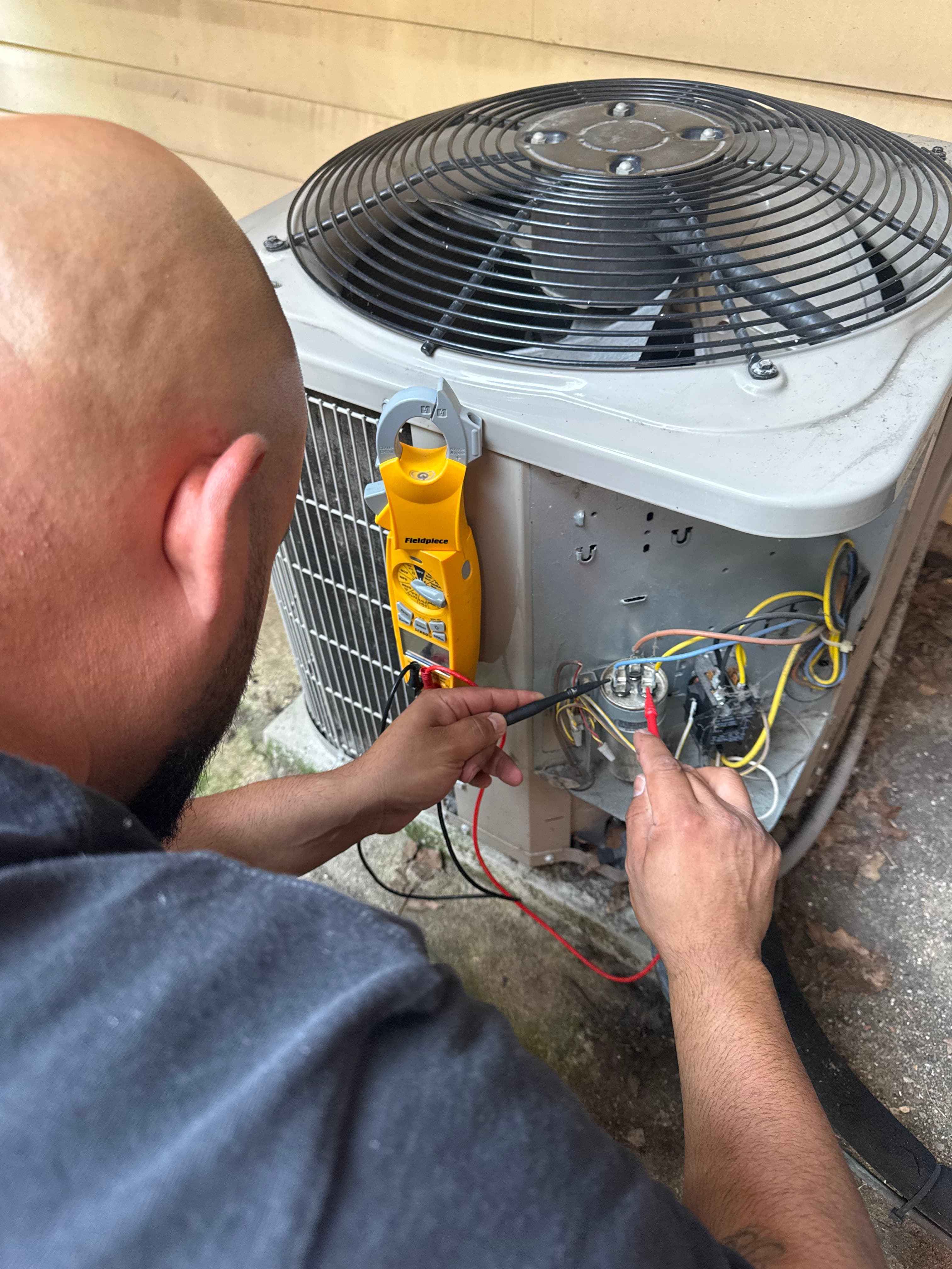 Technician uses a yellow multimeter to test the capacitor of an outdoor air conditioning unit.