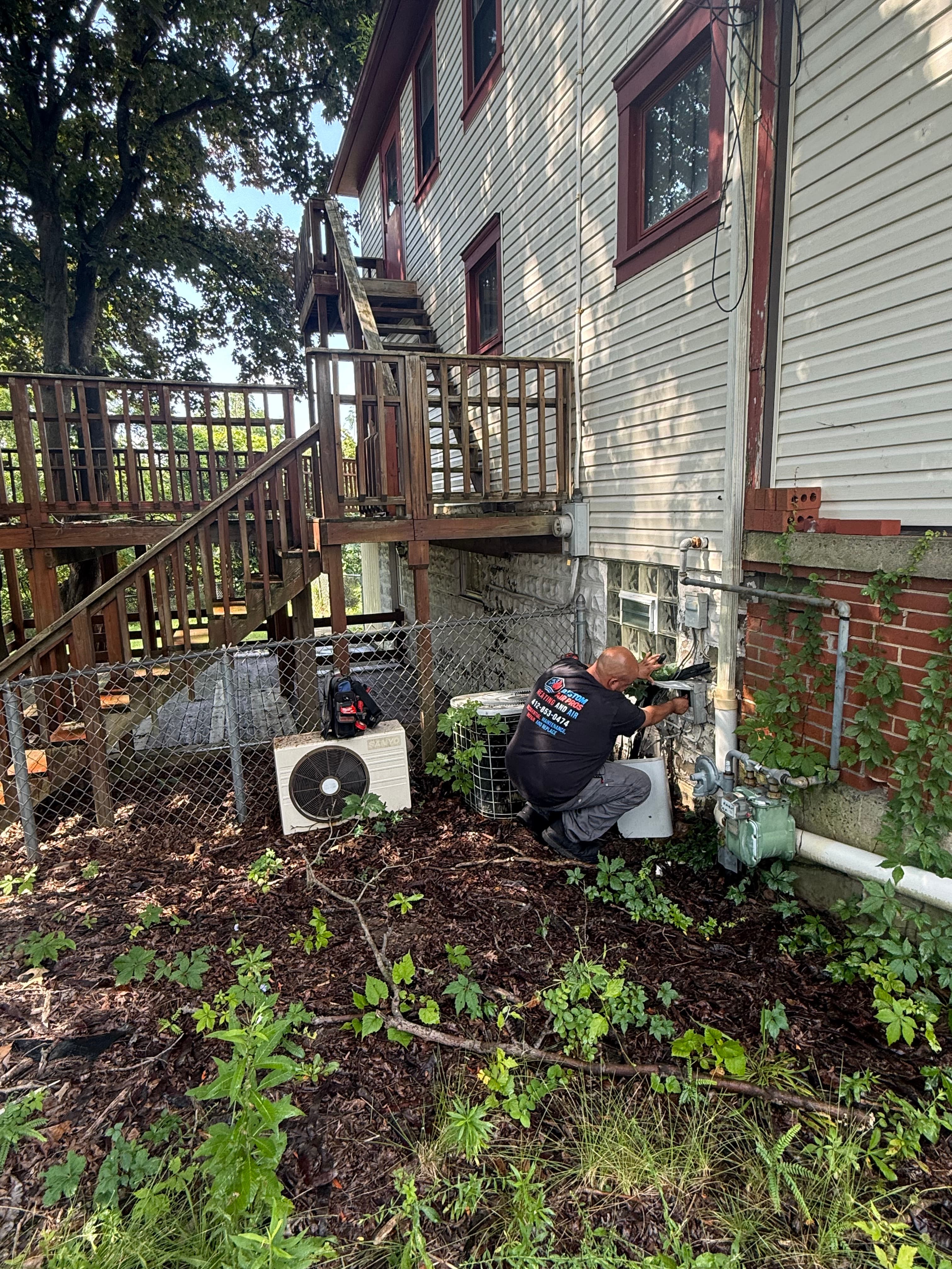 Technician repairs an outdoor air conditioning unit next to a house with a wooden deck.