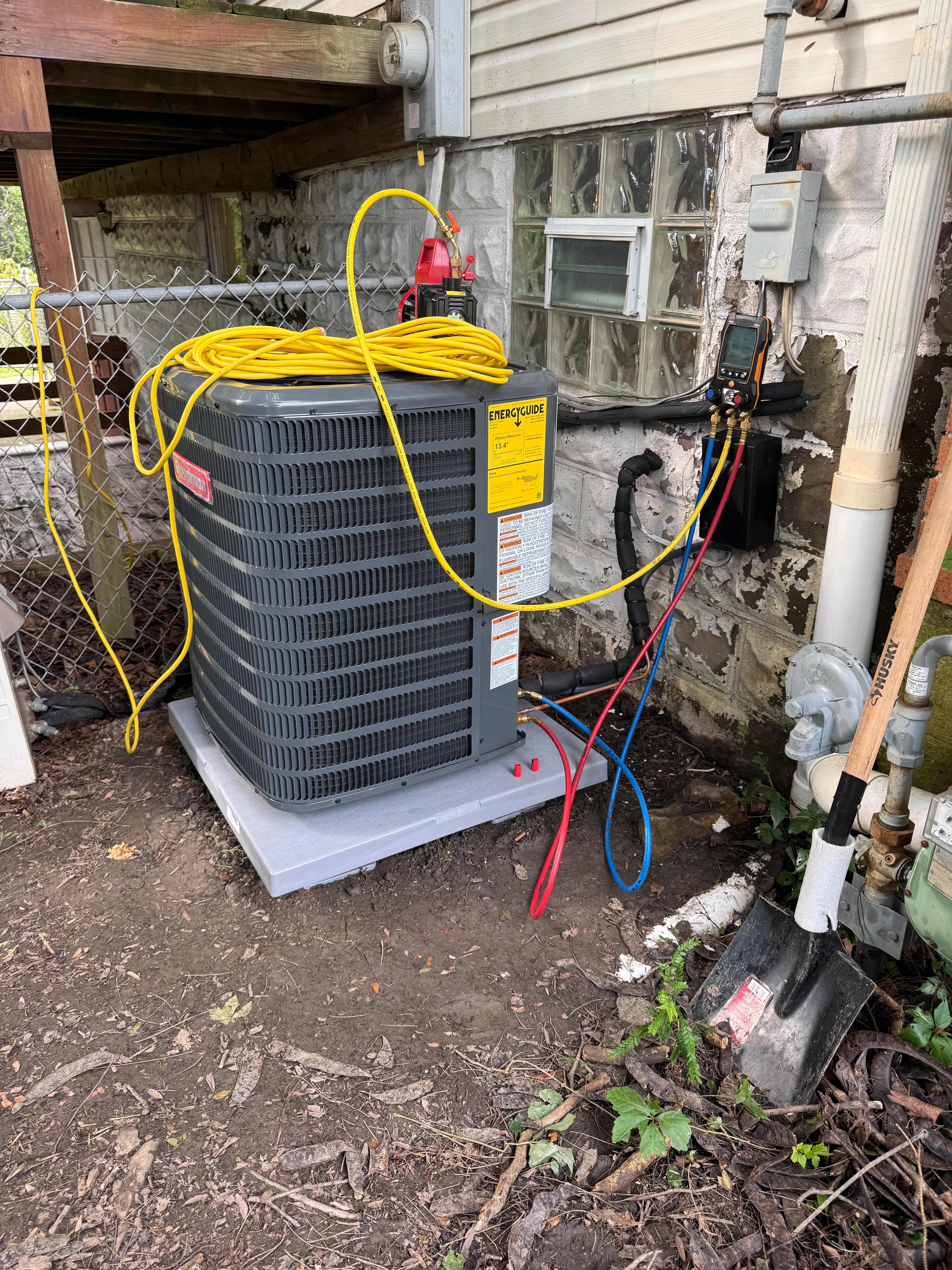 Goodman air conditioning condenser unit being serviced with yellow hoses and manifold gauges outdoors.