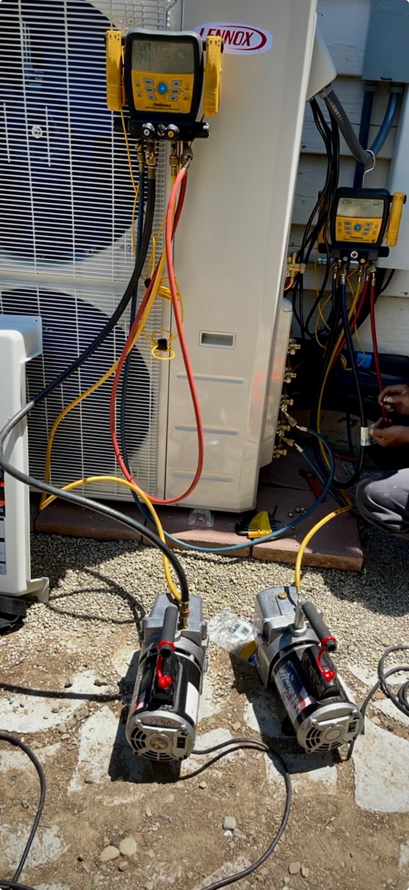 Vacuum pumps and digital manifold gauges connected to a Lennox outdoor HVAC unit.