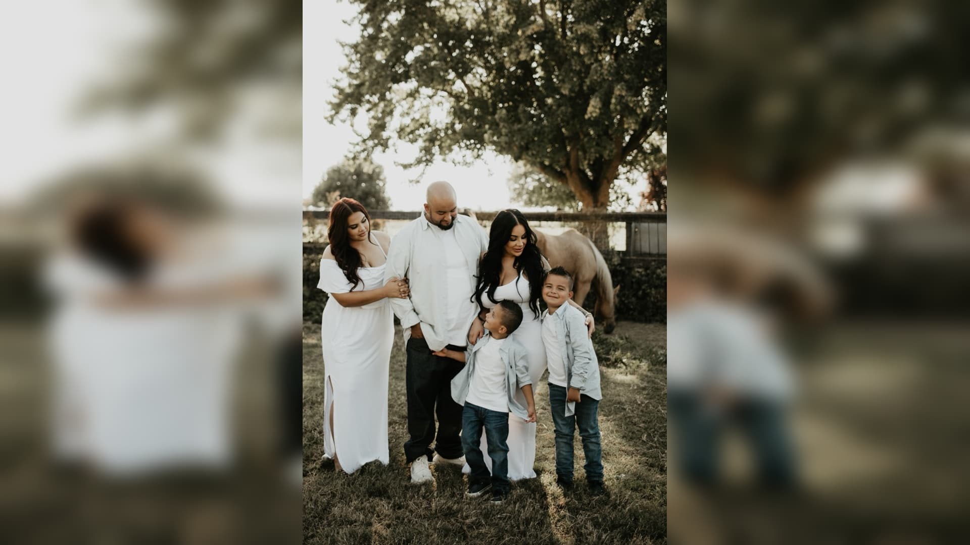 Family of five in white and blue attire posing outdoors with a horse behind them.