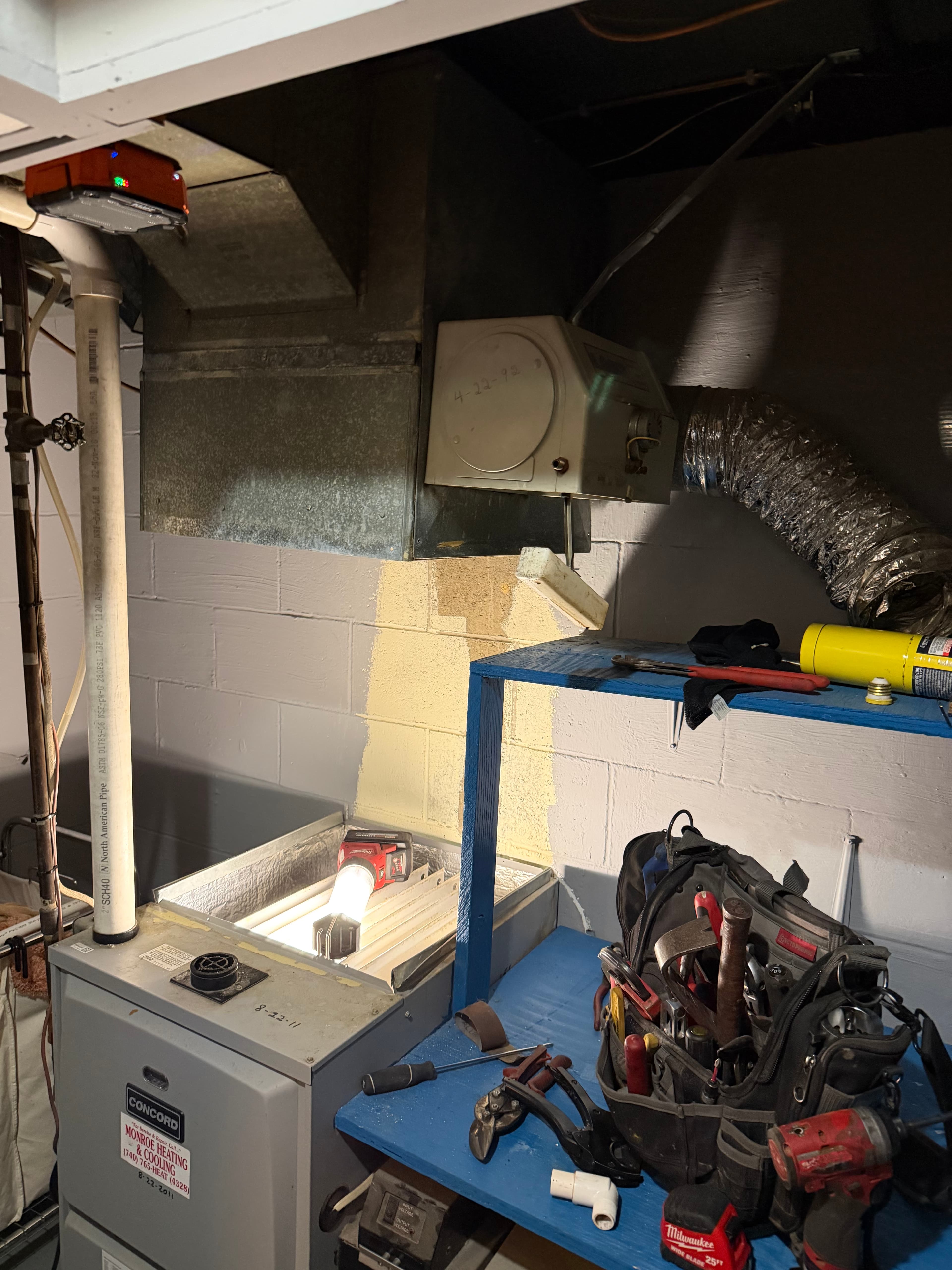 Basement furnace with a bright work light and various tools on a blue workbench.